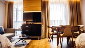 Habitació d'hotel moderna amb un sofà, una taula de dinar amb caires, una televisió i un armari.