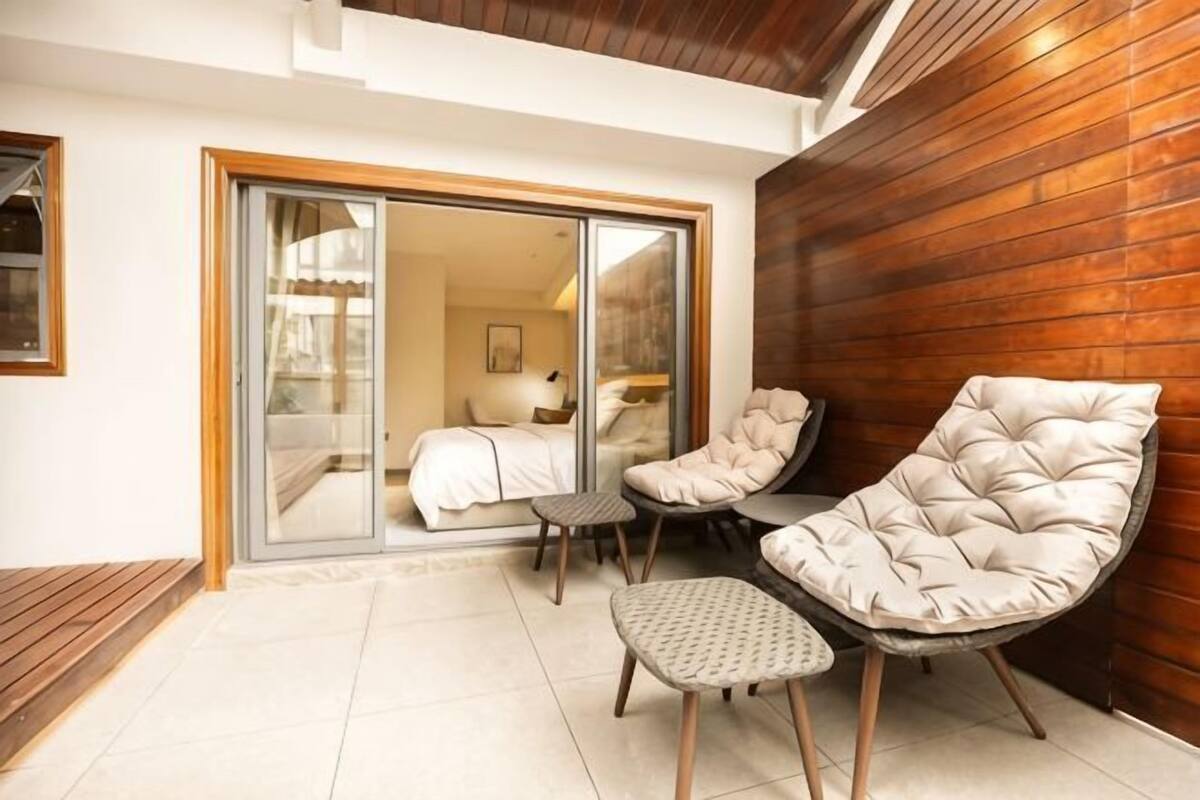 A room with a bed, a chair, a small table, and a sliding glass door leading to another room.