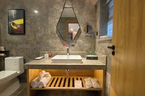 Un baño con un lavabo blanco, un espejo, un perchero para toallas y un estante de madera con toallas.