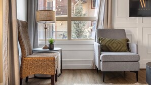 A cozy corner with a wicker chair, a grey armchair, a floor lamp, and a small table with a plant. - Blue Heron Pointe | Lakeview | Pool | Hot Tub |Gym (Invermere)