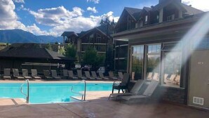 A pool area with lounge chairs and a hot tub, surrounded by buildings with large windows. - Blue Heron Pointe | Lakeview | Pool | Hot Tub |Gym (Invermere)