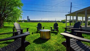 A grassy outdoor area with Adirondack chairs and a metal table, a covered pavilion, and a distant view of a bridge and buildings. - Speedway Luxe | Hot Tub | Shuffle | Steps to Track (Indianapolis)