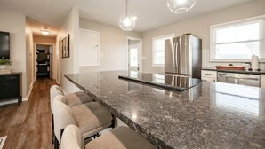 A modern kitchen with a granite countertop, stainless steel appliances, and pendant lighting. - Speedway Luxe | Hot Tub | Shuffle | Steps to Track (Indianapolis)