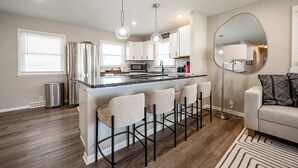 A modern kitchen with a central island, bar stools, stainless steel appliances, and pendant lighting. - Speedway Luxe | Hot Tub | Shuffle | Steps to Track (Indianapolis)