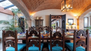 Uma sala de jantar com teto de tijolos, cadeiras de madeira com almofadas azuis e um lustre.