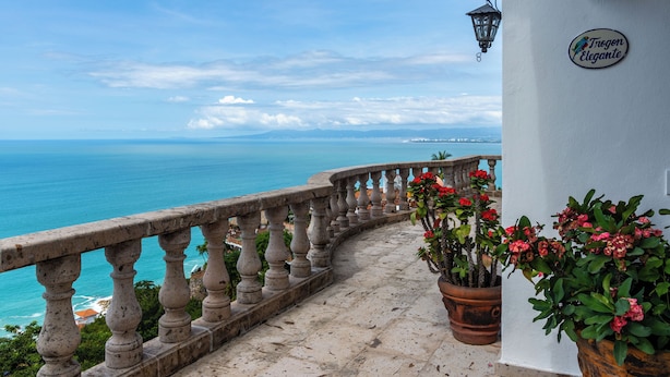 Uma varanda com vista para o mar, uma parede branca com uma placa e plantas em vasos.