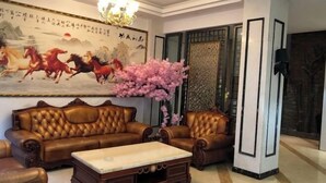 A room with a brown leather sofa set, a wooden coffee table, and a large painting of horses on the wall. - Ziranfeng Fashion Hotel (Congjiang Food Street) (Congjiang)
