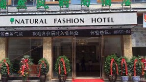 A hotel entrance with a sign reading "NATURAL FASHION HOTEL". There are potted plants with red ribbons in front of the entrance. - Ziranfeng Fashion Hotel (Congjiang Food Street) (Congjiang)