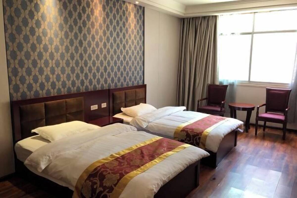 Een hotelkamer met twee bedden, een houten hoofdbord, een tafeltje en een stoel.