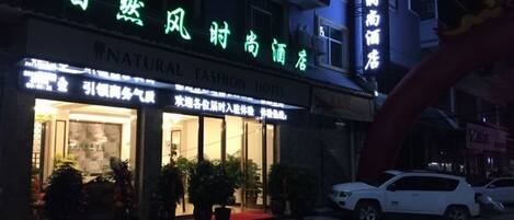 A hotel with a sign in a foreign language, a red carpet entrance, and a white car parked outside.