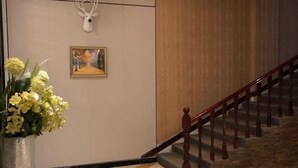 A hallway with a wooden staircase, a deer head mounted on the wall, and a framed painting. - Ziranfeng Fashion Hotel (Congjiang Food Street) (Congjiang)