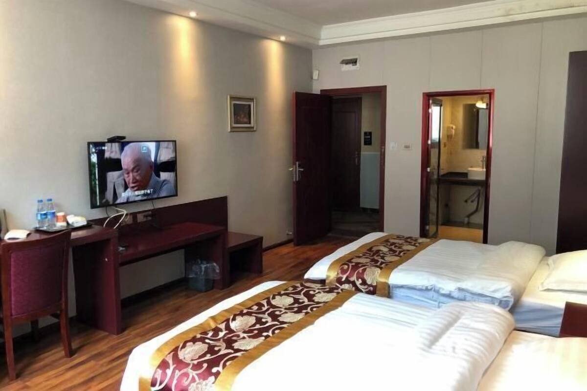 Een hotelkamer met twee bedden, een bureau, een televisie en een badkamer die door een open deur zichtbaar is.