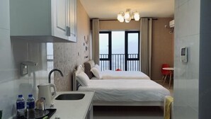 A hotel room with a kitchenette, a bed, a small table, and a balcony with curtains. - Meet Sunshine Holiday Apartment (Zhuhai Hengqin) (Zhuhai)