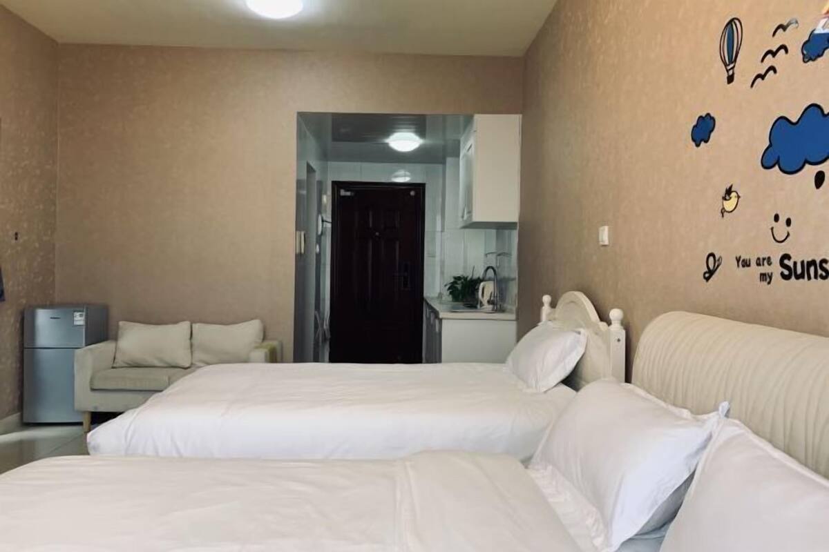 Une chambre d’hôtel avec deux lits, une kitchenette et une salle de bain visible à travers une porte ouverte.