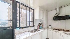 A kitchen with white cabinets, a double sink, and a window with a view of tall buildings. - Meet Sunshine Holiday Apartment (Zhuhai Hengqin) (Zhuhai)