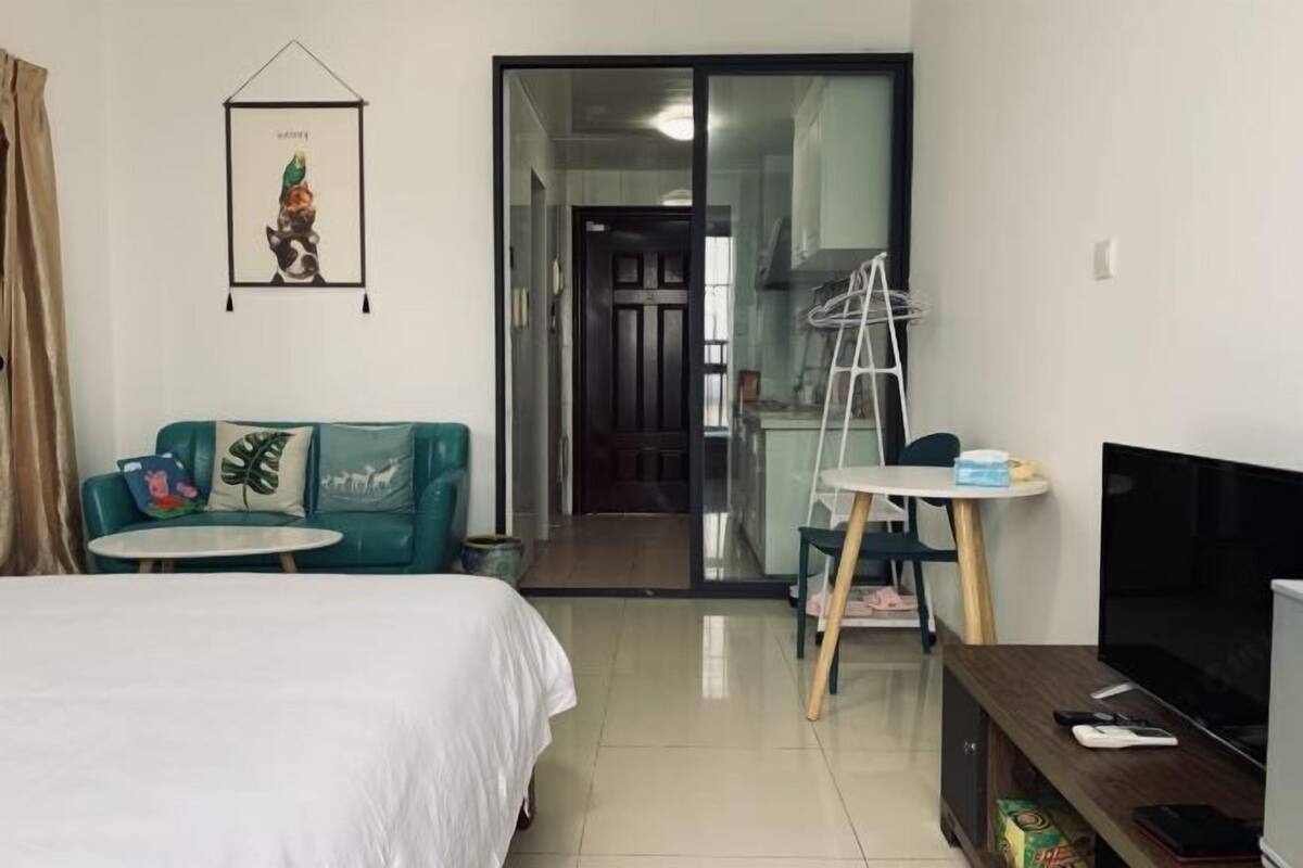 Une chambre d’hôtel avec un lit, un canapé vert, une petite table, une télévision et une porte donnant sur un balcon.