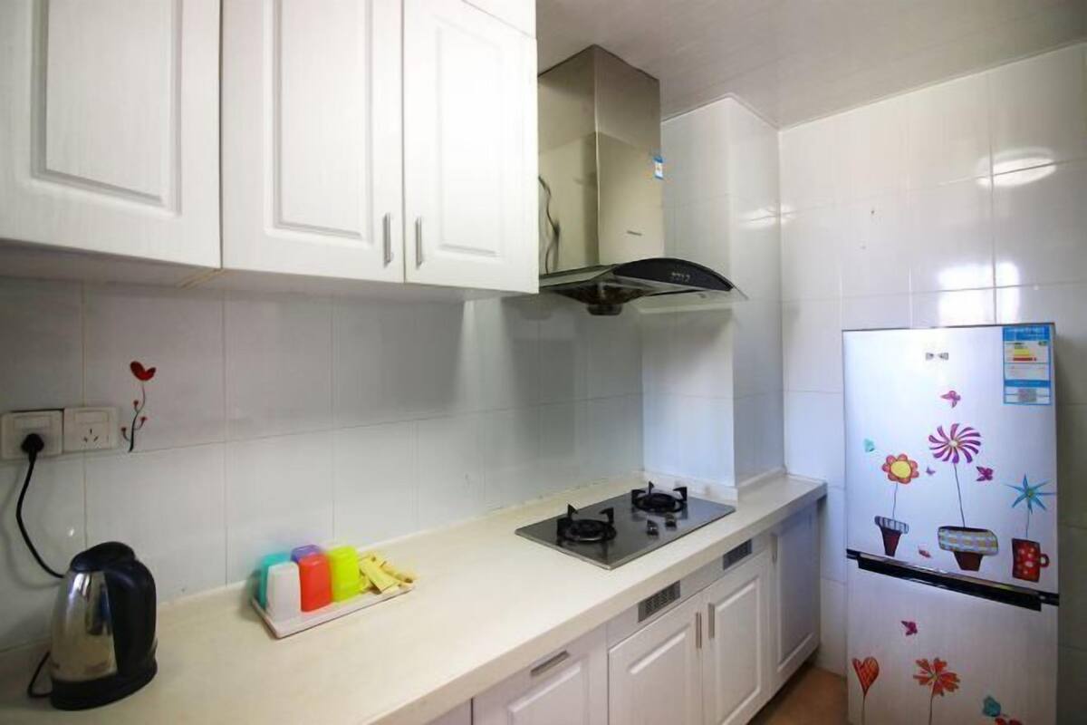 Une cuisine avec des meubles blancs, une cuisinière noire et un réfrigérateur décoré d’aimants colorés.
