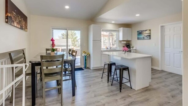 A modern kitchen with a central island, a dining area with a table and chairs, and a view of the outdoors. - Gameroom and Theater in a breathtaking home (Centennial)