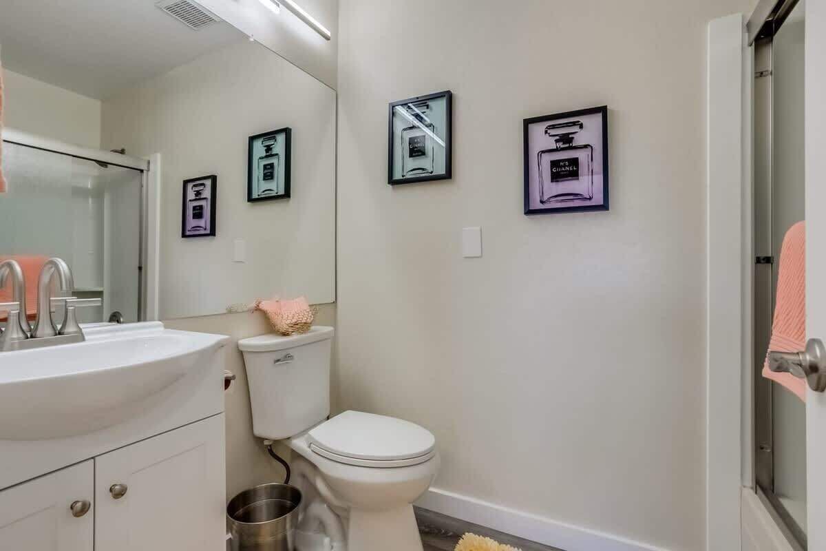 Un baño con lavamanos blanco, inodoro y zona de ducha. Hay cuadros enmarcados en la pared.