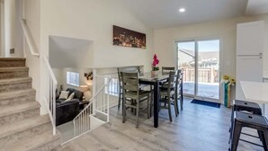 A spacious living area with a staircase, a dining table with chairs, a sofa, and a cityscape painting on the wall. - Gameroom and Theater in a breathtaking home (Centennial)