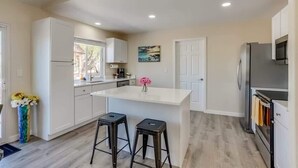 A modern kitchen with white cabinetry, a central island with stools, a refrigerator, and a microwave. - Gameroom and Theater in a breathtaking home (Centennial)