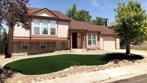 A two-story house with a stone facade, a front yard with a green lawn, and a garage. - Gameroom and Theater in a breathtaking home (Centennial)