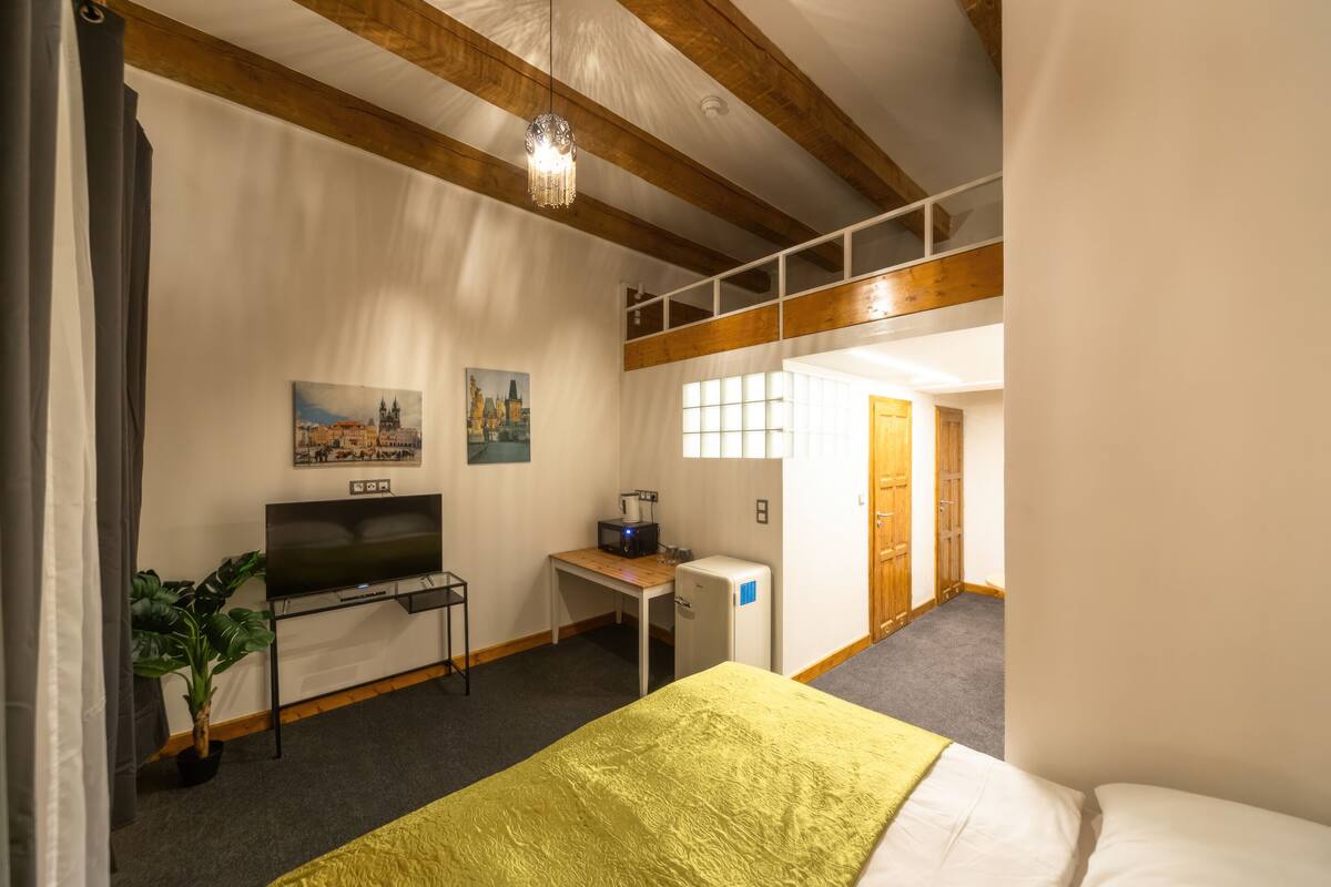 Ein Schlafzimmer mit Bett, Schreibtisch, Fernseher, Pflanze und Fenster.