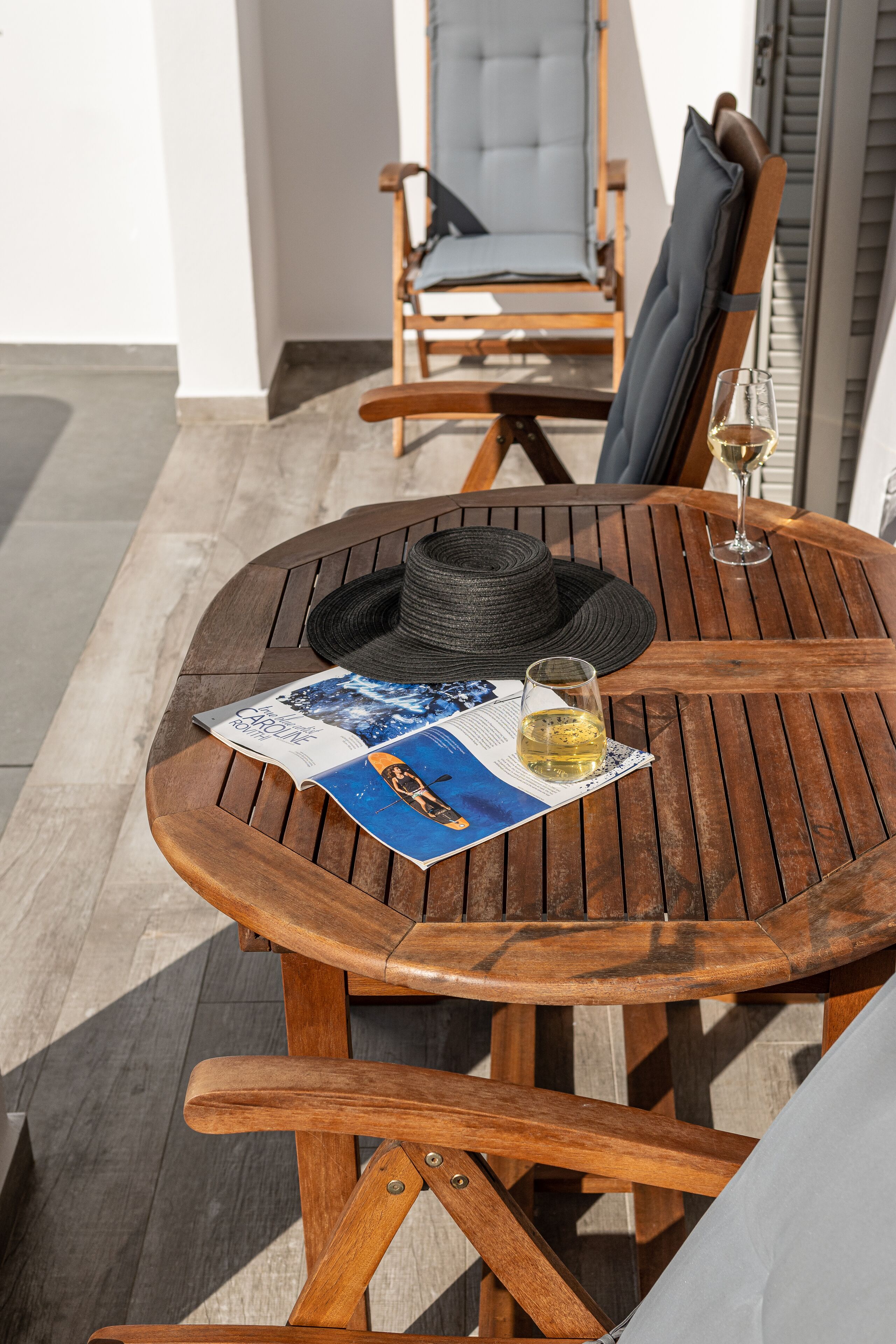 Una mesa de madera con una revista, un sombrero y una copa de vino.
