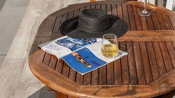 Una mesa de madera con una revista, un sombrero y una copa de vino.