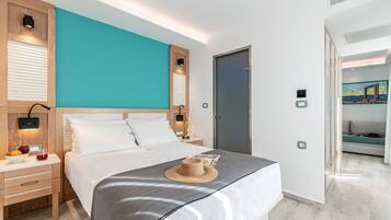 Una habitación de hotel moderna con una cama grande, cabecera de madera y una pared de acento color turquesa. Hay una mesita de noche con una lámpara y un frutero.