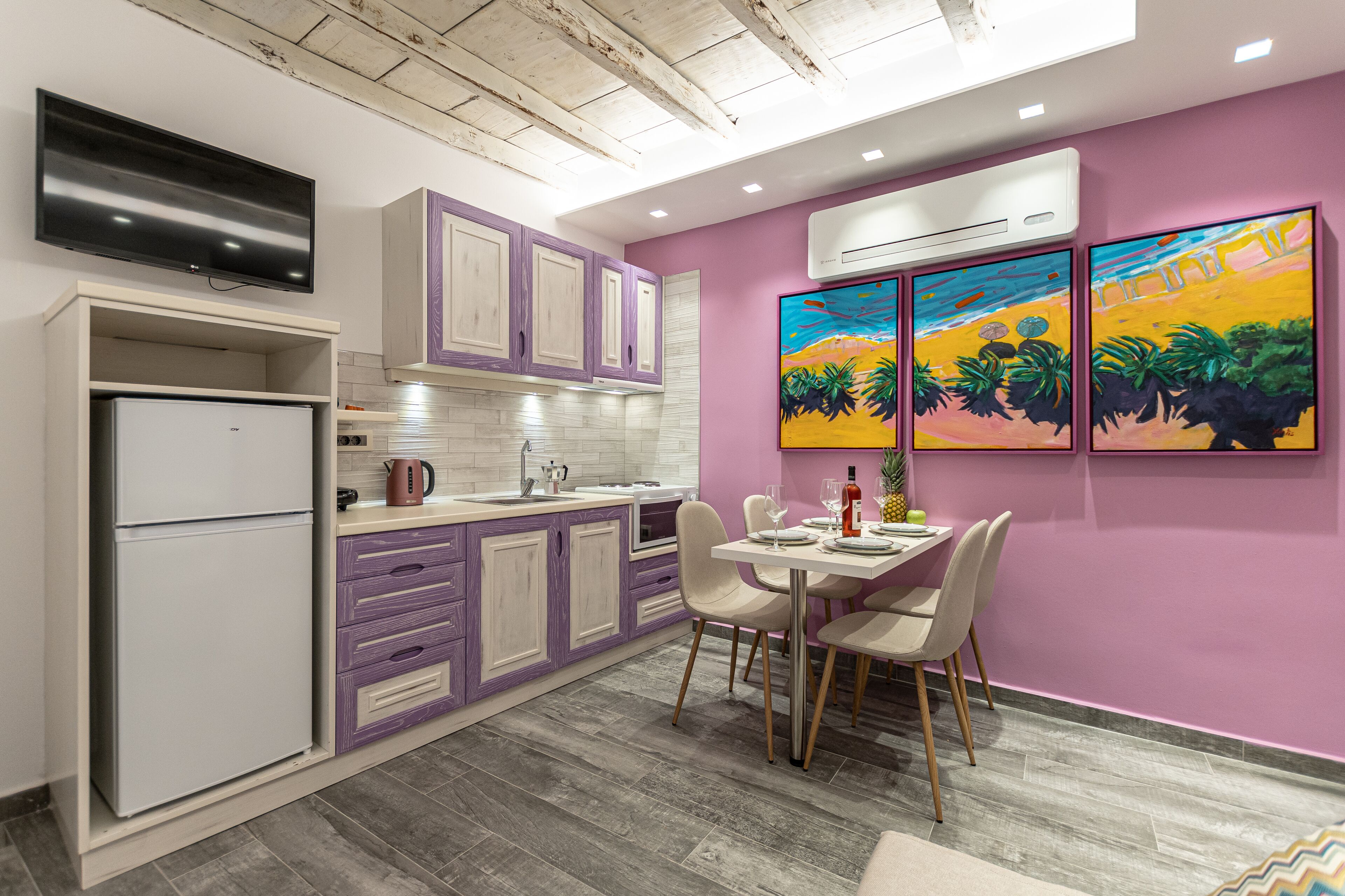 A modern kitchen with a dining area, featuring a built-in refrigerator, white cabinets, a purple dining table, and a colorful mural on the wall.