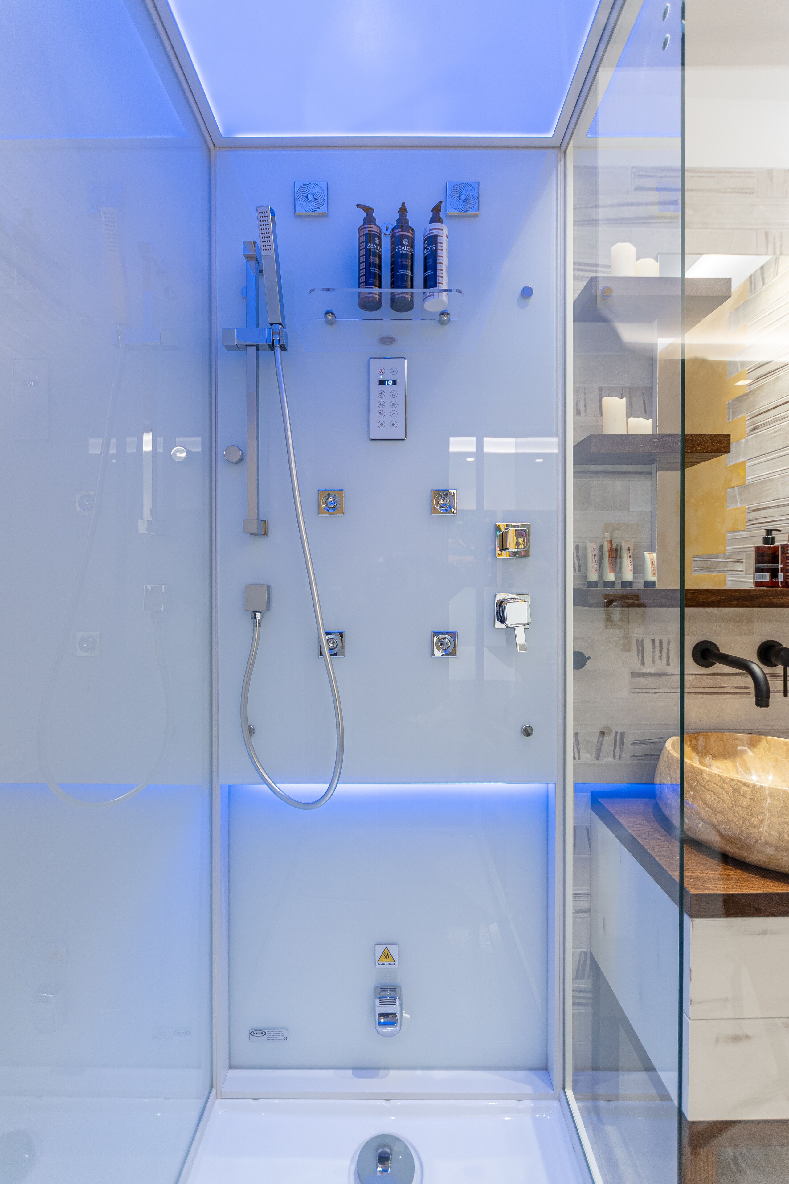 Een moderne badkamer met een glazen douchecabine, een ingebouwd wastafelmeubel en een douche met meerdere bedieningspanelen.