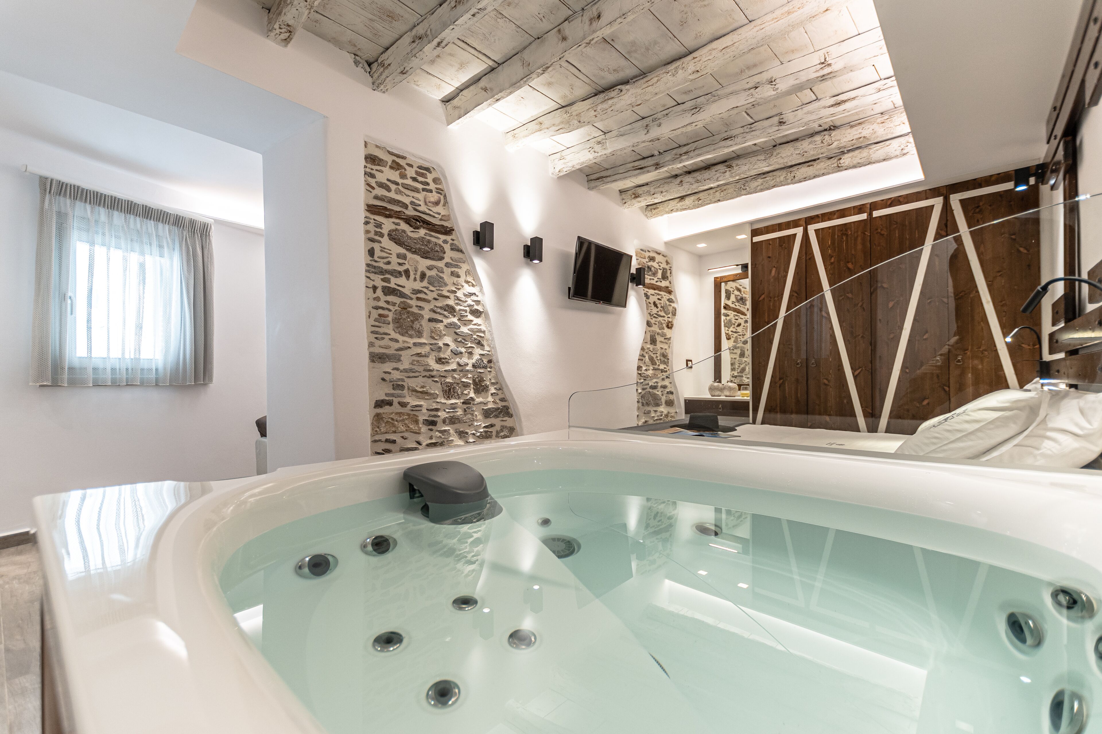 Un baño moderno con una bañera grande, pared de piedra, paneles de madera y techo con vigas a la vista.