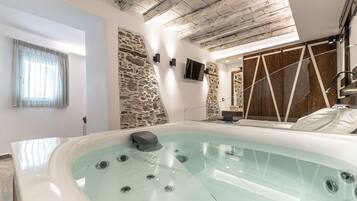 Un baño moderno con una bañera grande, pared de piedra, paneles de madera y techo con vigas a la vista.
