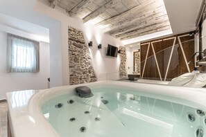 A modern bathroom with a large bathtub, stone wall, wooden paneling, and a ceiling with exposed beams.
