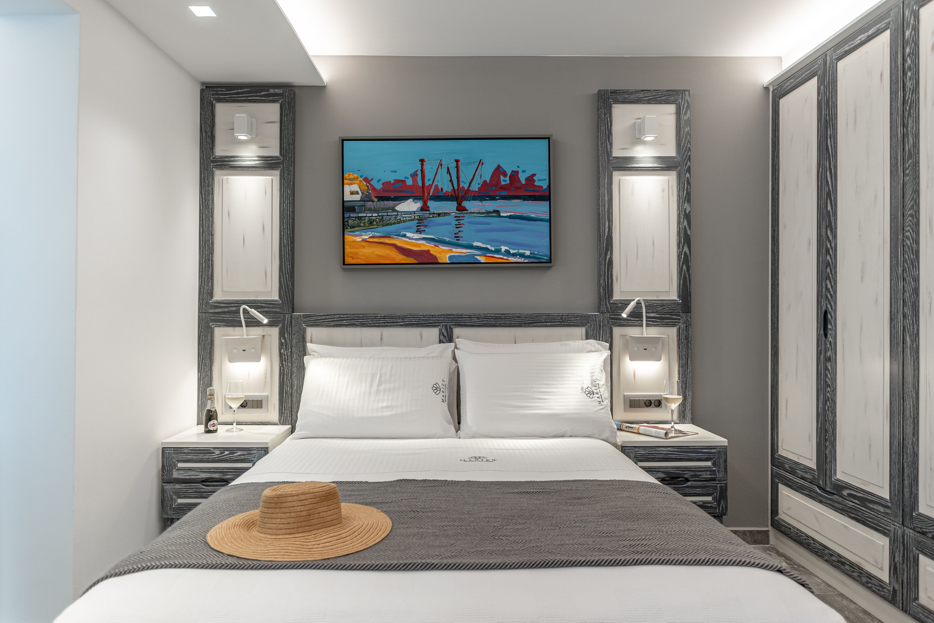 A modern hotel room with a large bed, two bedside tables with lamps, a painting on the wall, and a cityscape view.