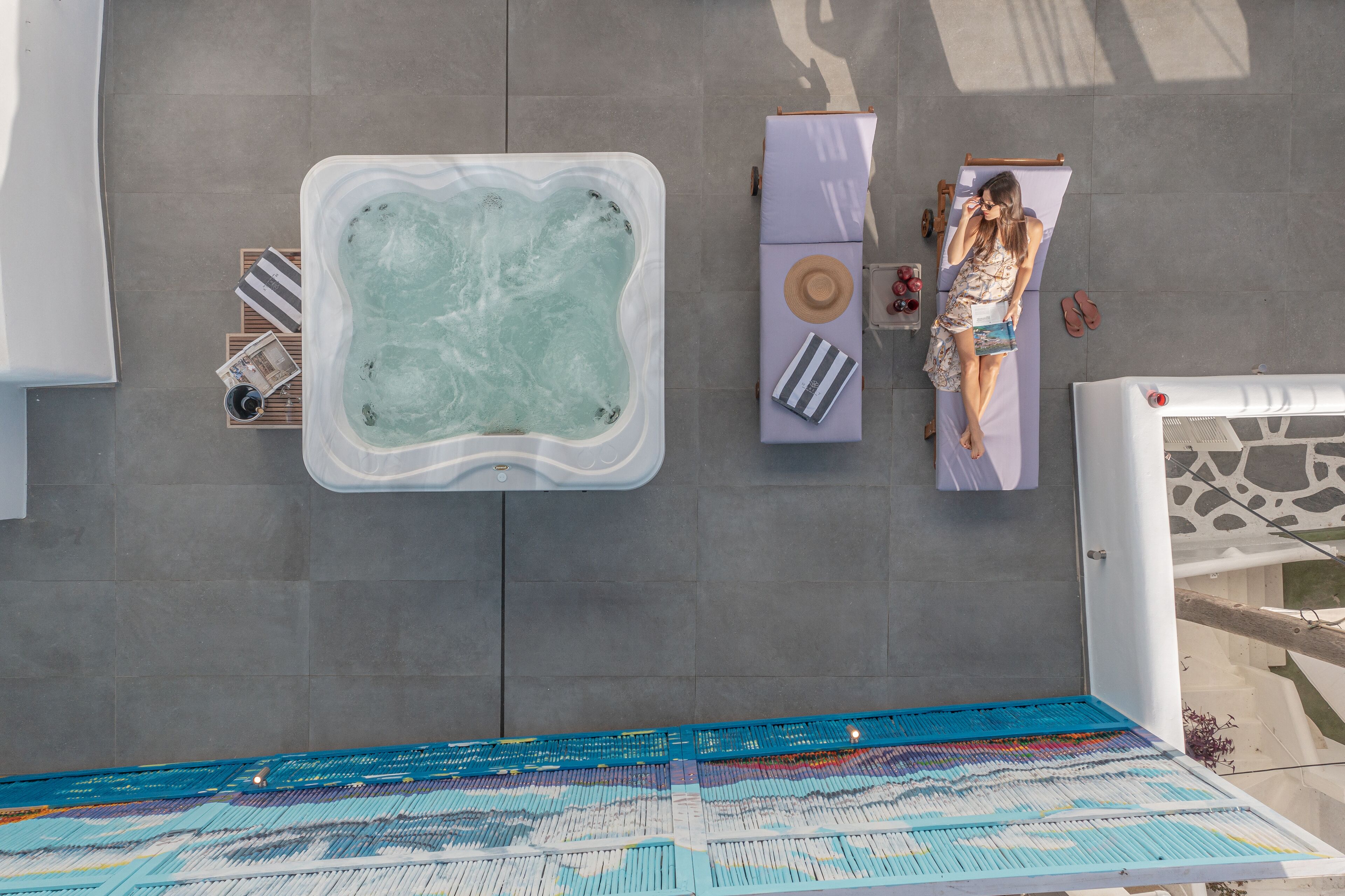 An aerial view of a rooftop pool area with a hot tub, lounge chairs, and a patterned floor.