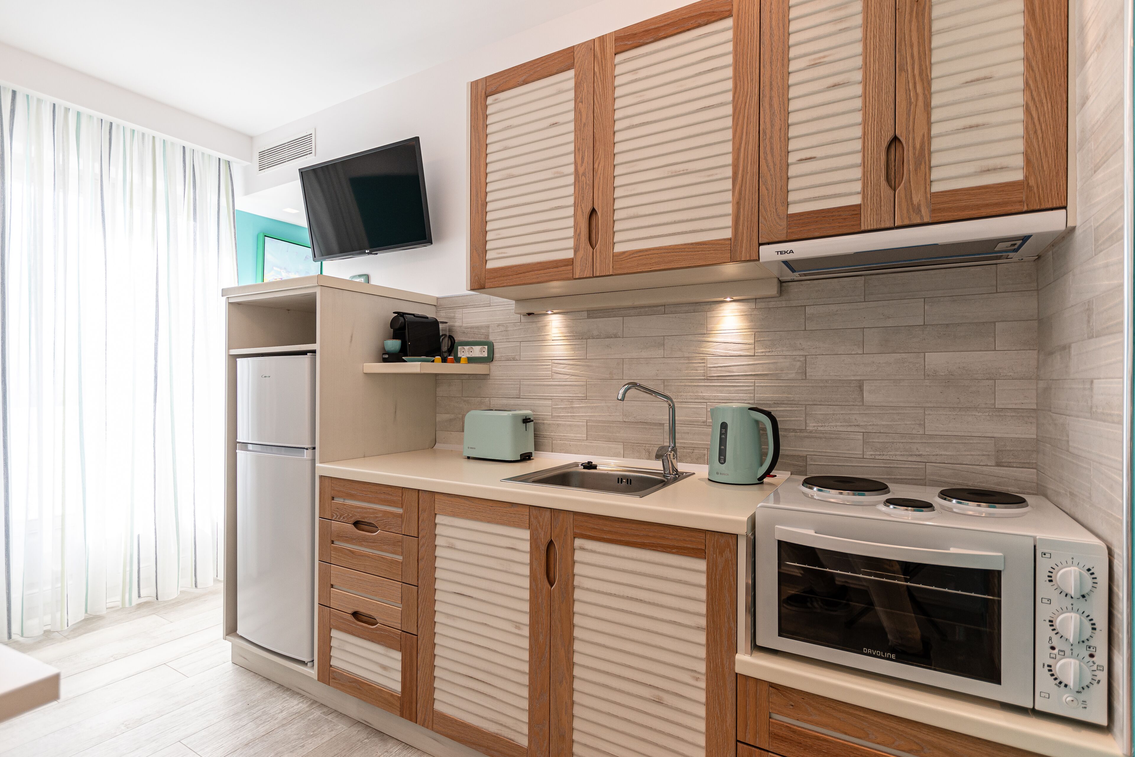 Una cocina moderna con gabinetes de madera, horno empotrado, un lavamanos y un televisor de pantalla plana montado sobre la encimera.