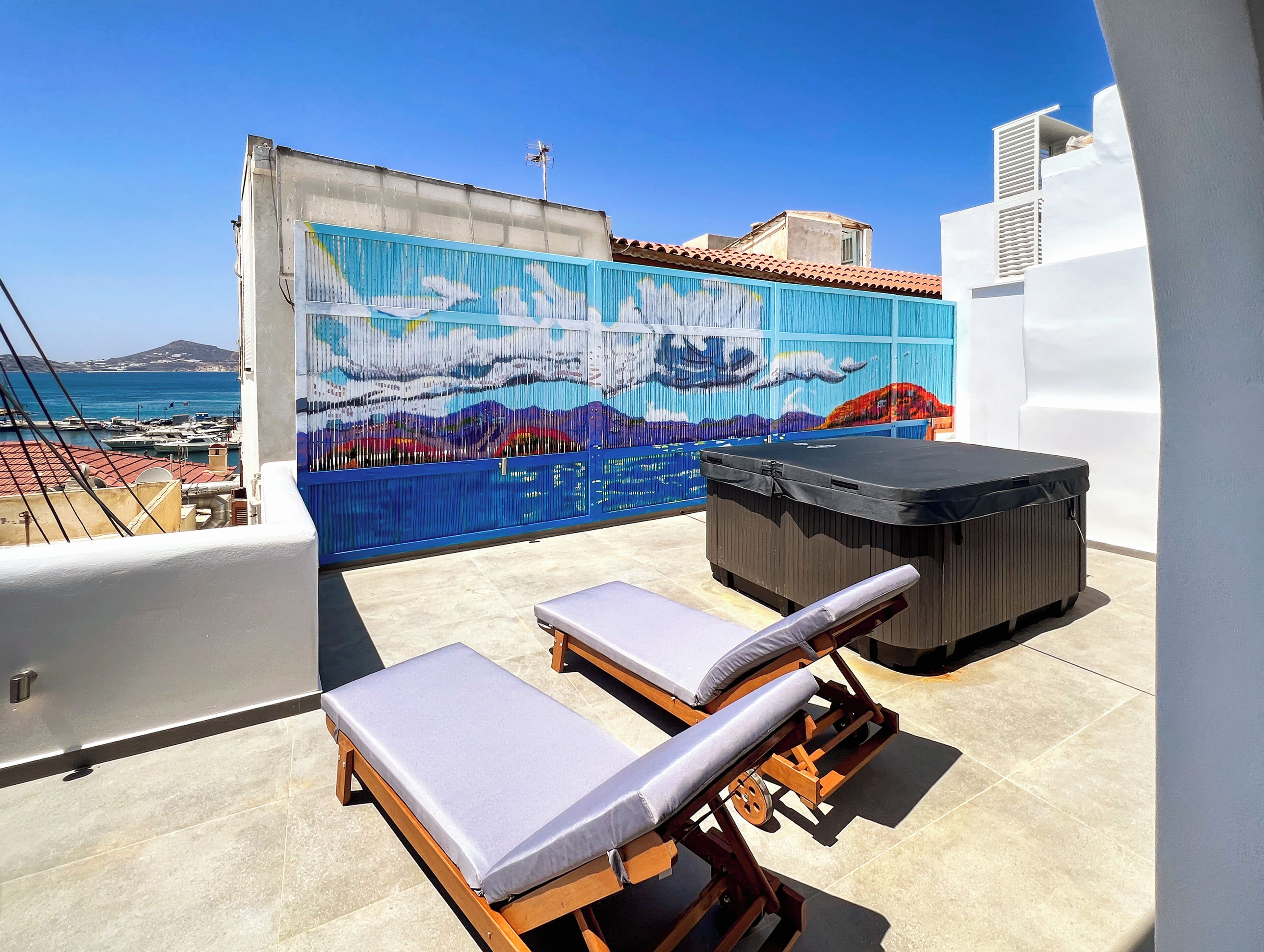 Una terraza en la azotea con dos tumbonas, un jacuzzi y un mural.