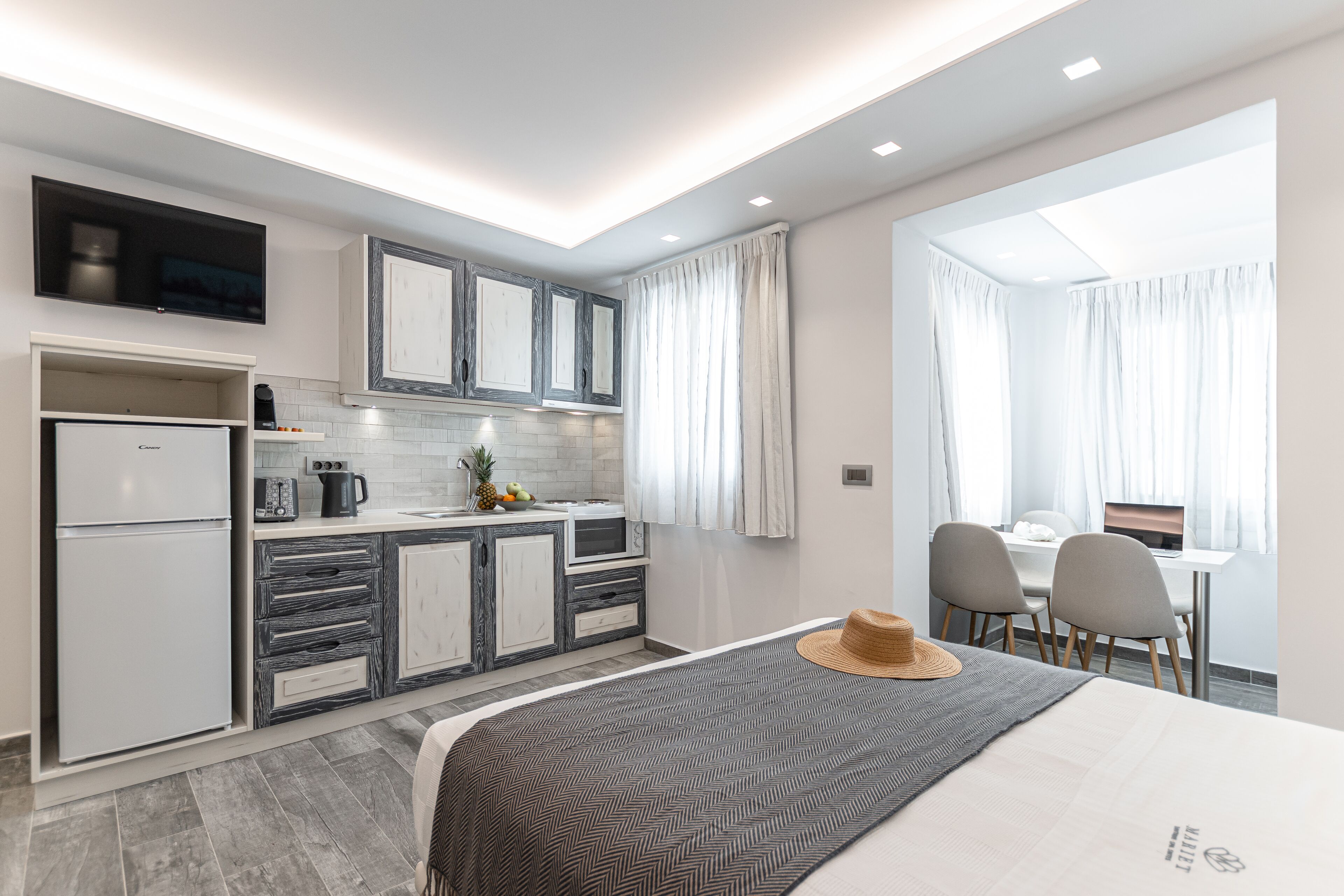 A modern hotel room with a kitchenette, a dining area, and a large window.