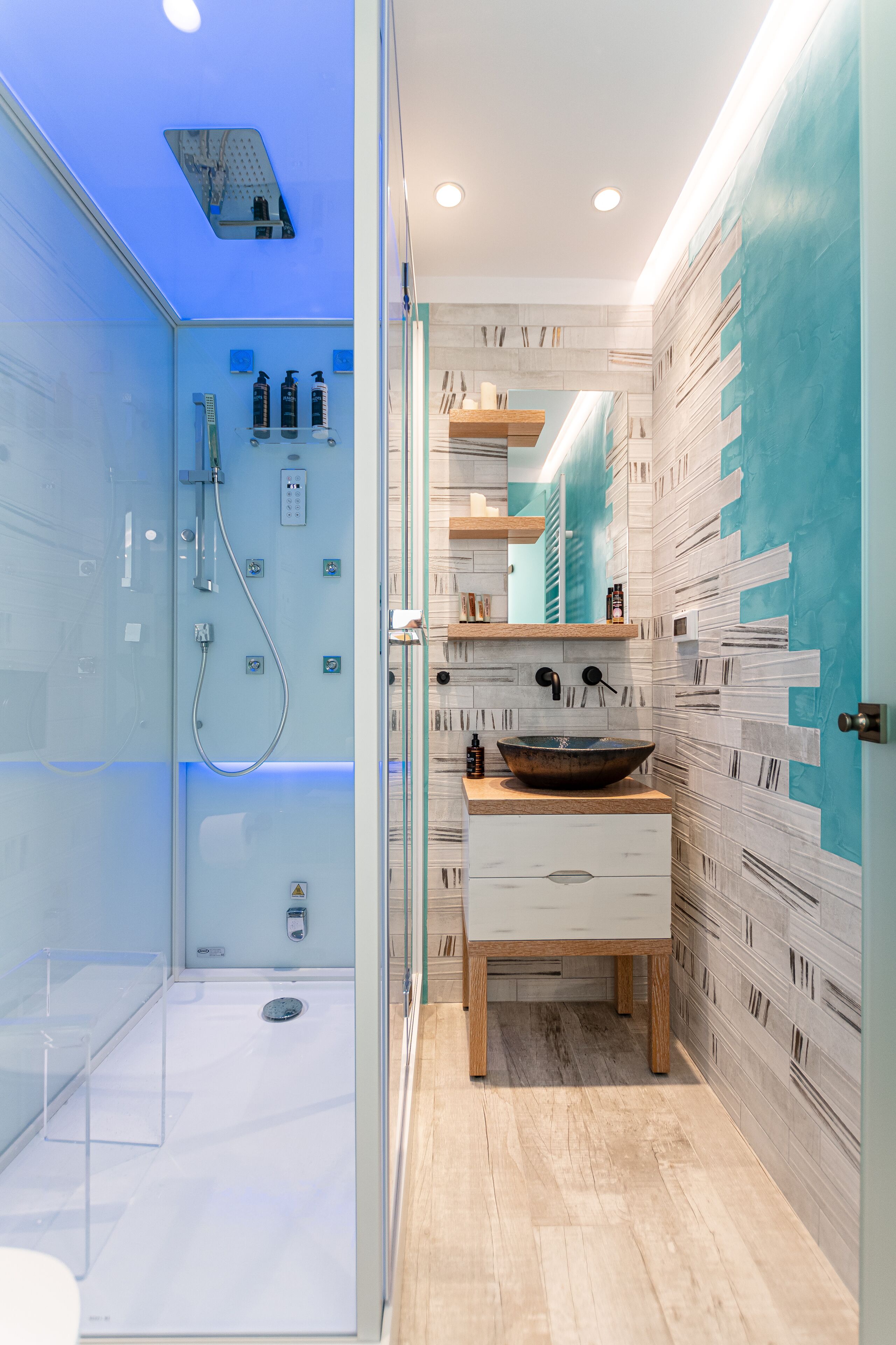 Un baño moderno con ducha de vidrio, tocador de madera con un lavamanos grande y salpicadero de azulejos.