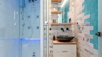 Un baño moderno con ducha de vidrio, tocador de madera con un lavamanos grande y salpicadero de azulejos.