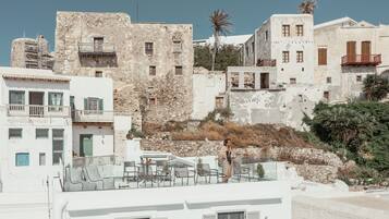 Um edifício à beira-mar com paredes de pedra, varandas e um terraço com mobiliário de exterior.