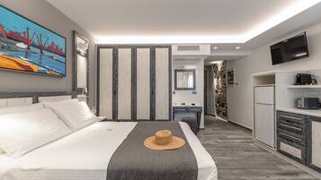 A hotel room with a bed, a desk, a kitchenette, and a TV.