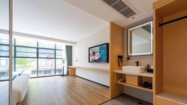 Moderni hotellihuone, jossa on suuri ikkuna, sänky, puinen peilipöytä ja seinällä oleva kehystetty taulu.