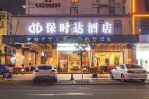 Ein Hotel mit auffälliger Beschilderung in einer Fremdsprache, einem gut beleuchteten Eingang und parkenden Autos davor.
