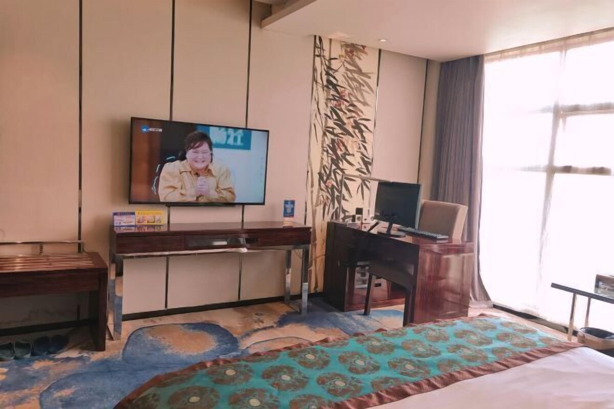 Ein Hotelzimmer mit Bett, Schreibtisch, Fernseher und einem großen Fenster.