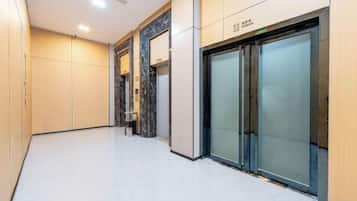 A hallway with a glass elevator, a reception desk, and a sign indicating the location.