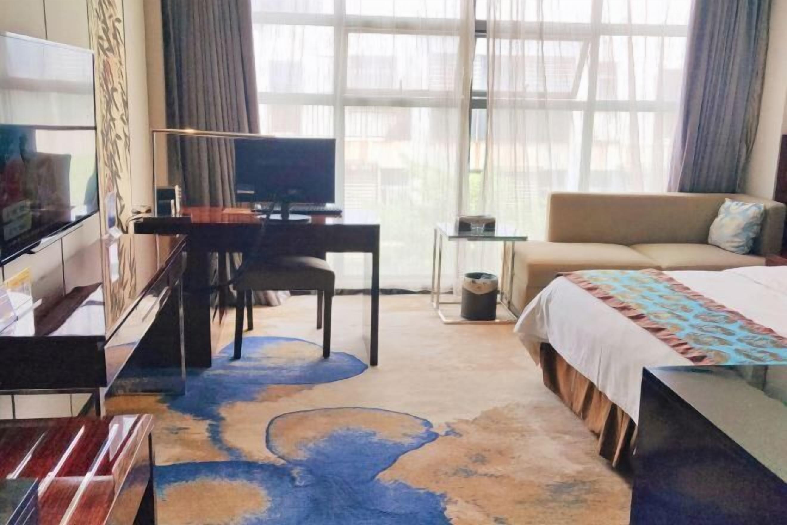 Una habitación de hotel con una cama, un escritorio con una silla, un televisor y un ventanal con cortinas.