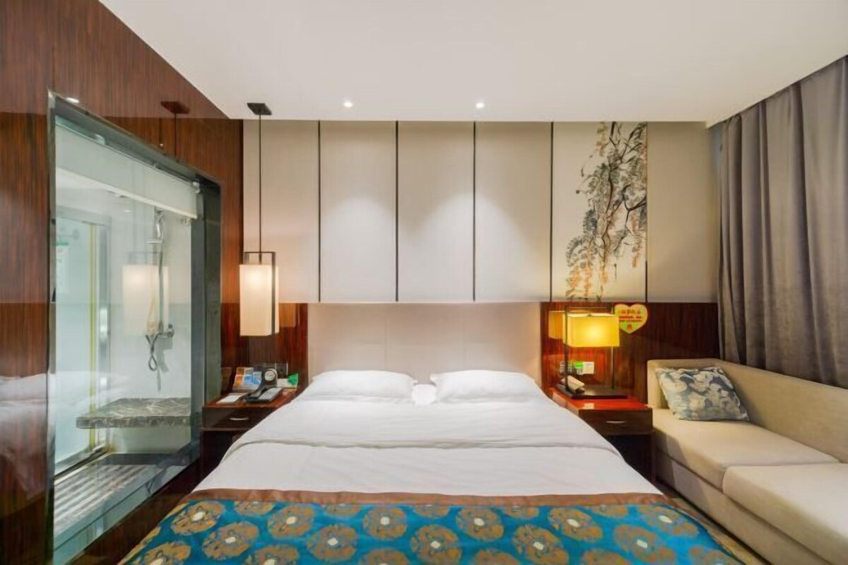 Ein Hotelzimmer mit einem großen Bett, einer Schlafcouch, einer Duschkabine aus Glas und einem Wandbild.